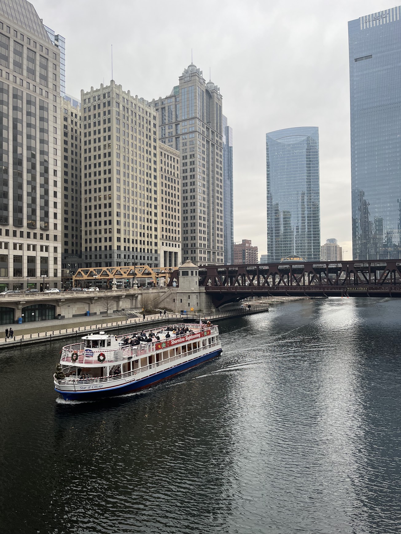 A view from a bridge overlooking the Chicago river, with a tour ferry floating by.