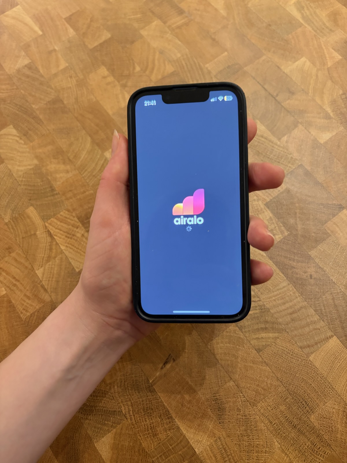 A hand holding an iPhone displaying the Airalo mobile app.